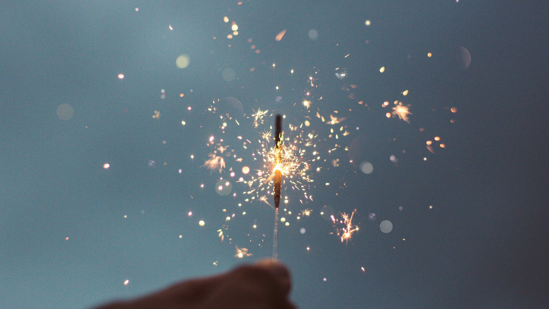 A hand holding a sparkler against the sky