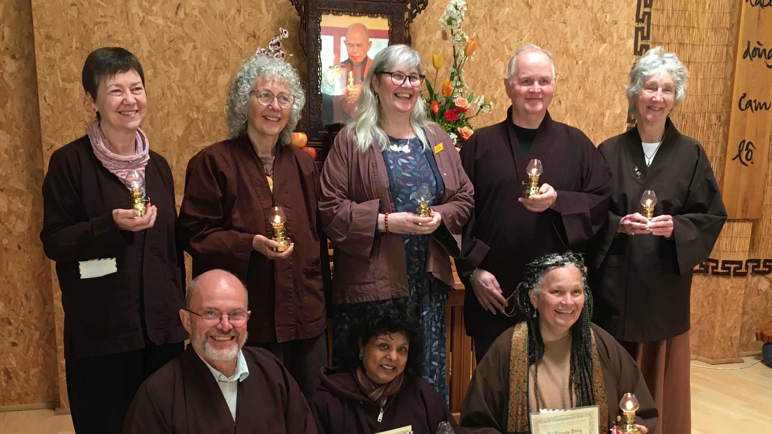 8 Dharma Teachers in brown jackets holding lamps